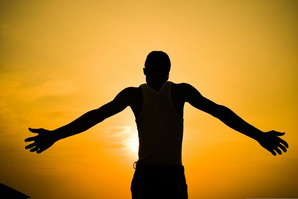 A mesmerizing silhouette of a man with outstretched arms against a golden sunset sky, encapsulating freedom and tranquility.